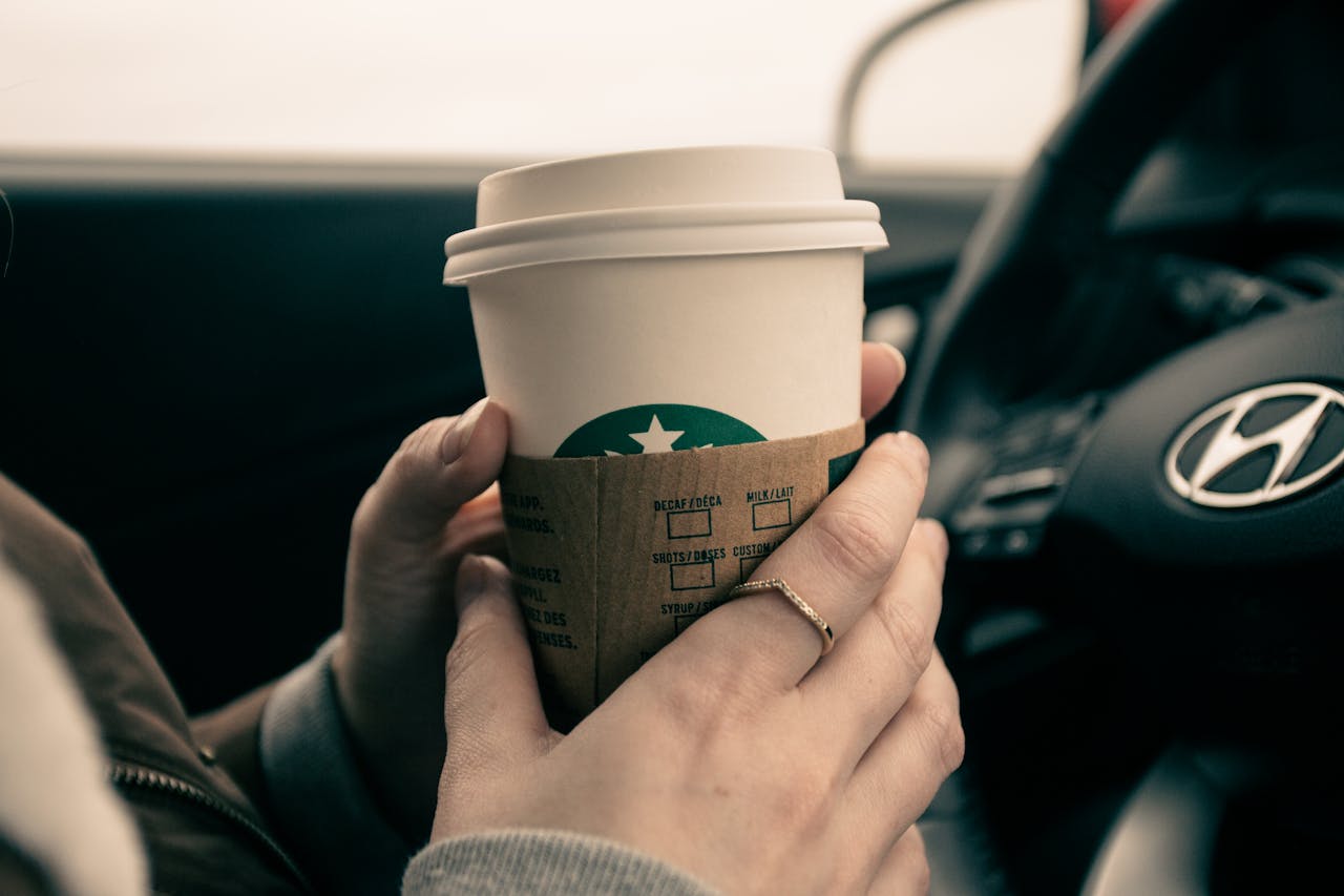 Close-up of hands holding a coffee cup inside a car, showcasing a modern lifestyle moment.