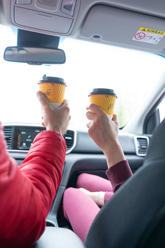 Couple holding takeaway coffee cups inside a car, capturing travel vibes.