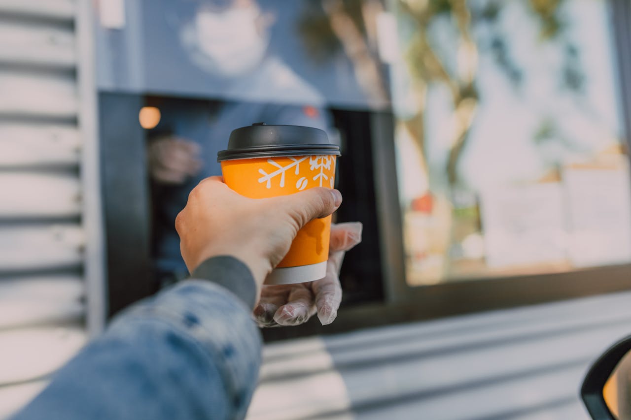 Hand reaching out for a hot coffee cup at a drive-thru window, depicting everyday convenience.